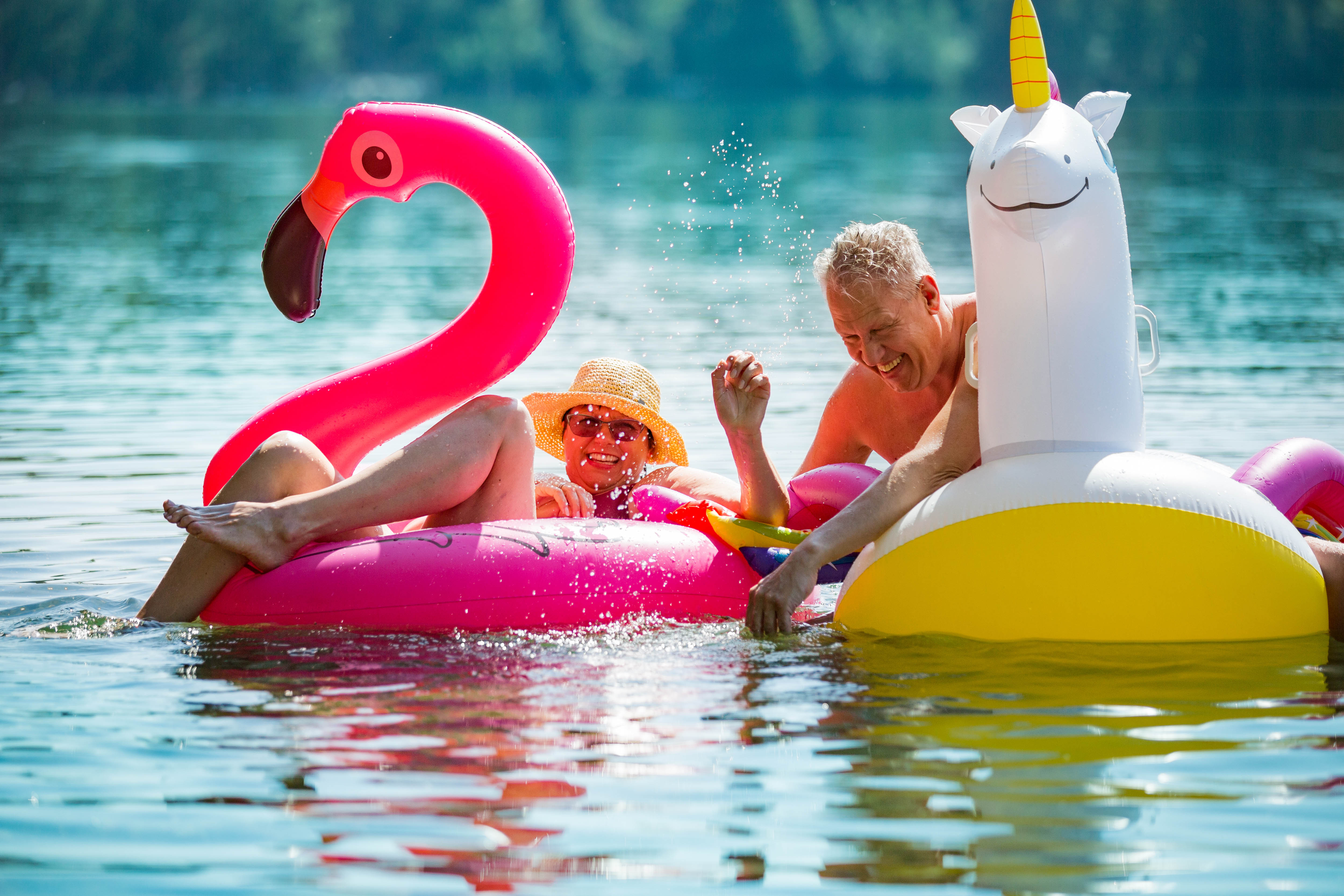 Older man and woman floating on flamingo and unicorn floaties in a lake